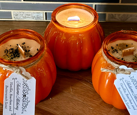 Three pumpkin-shaped candles on a wooden surface with visible labels.