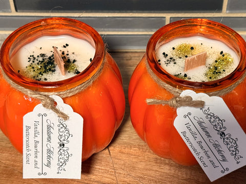 Two orange pumpkin-shaped candles with decorative tags on a wooden surface.