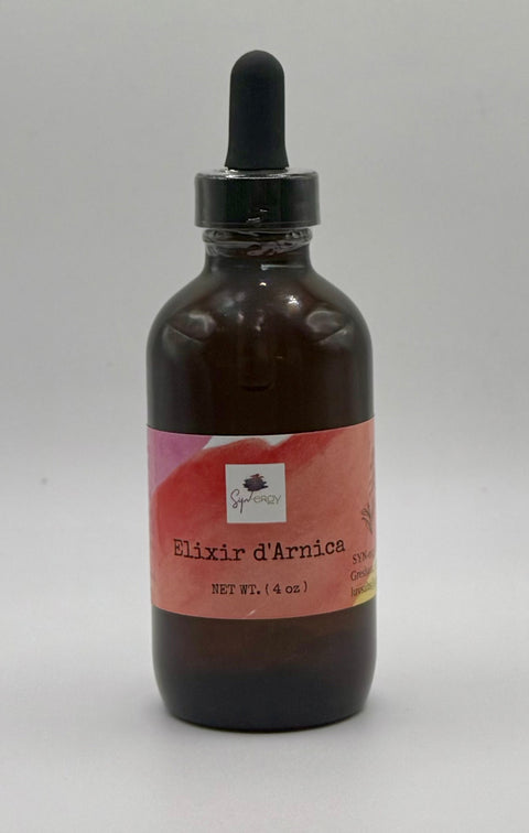 Glass bottle of arnica oil infused with rose quartz crystals, set against a natural background with soft lighting.
