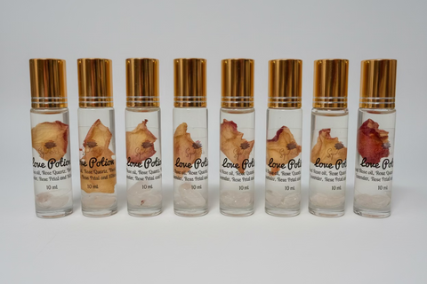 Set of eight small glass bottles with gold caps and dried flowers, labeled 'Love Potion', on a white surface.