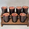 Set of seven Botanica Coconut Soy wax candles that are pink in black metallic vessels with rose petals and lavender on top.