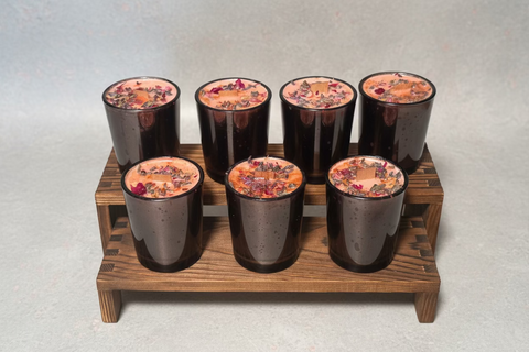 Set of seven Botanica Coconut Soy wax candles that are pink in black metallic vessels with rose petals and lavender on top.