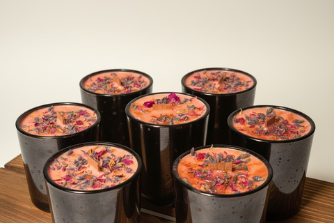 Decorative candles with floral elements in black holders on a wooden surface.