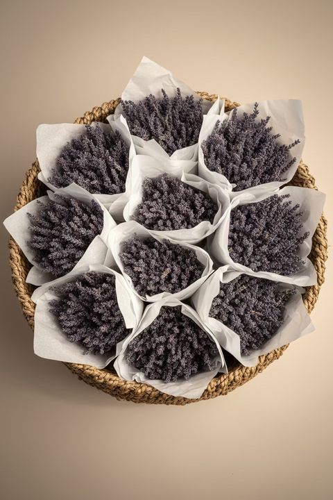  Loose bunches of dried lavender stems wrapped in white tissue paper, arranged inside a cardboard box.