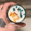 Hand holding a candle with blue apatite and frankincense resin in coconut soy wax base.