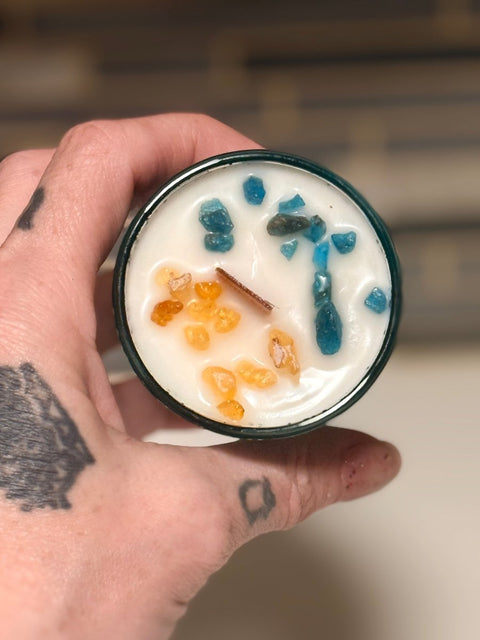Hand holding a candle with blue apatite and frankincense resin in coconut soy wax base.